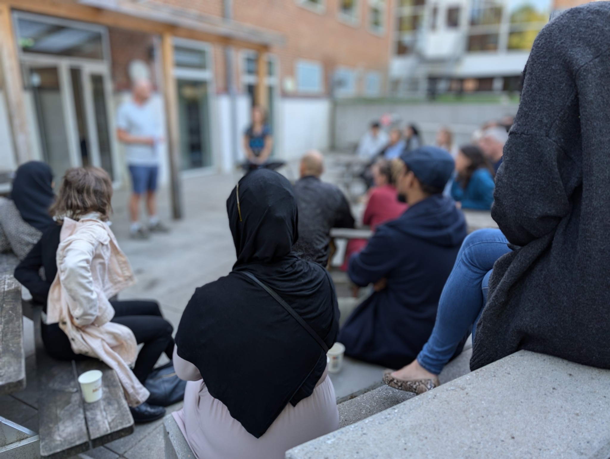 Mennesker sidder og lytter i skolegården
