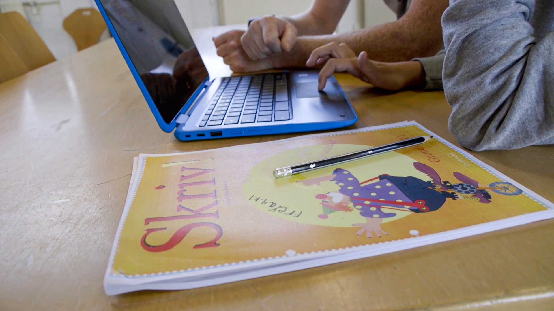 En voksen og en elev med en Chromebook og et hæfte