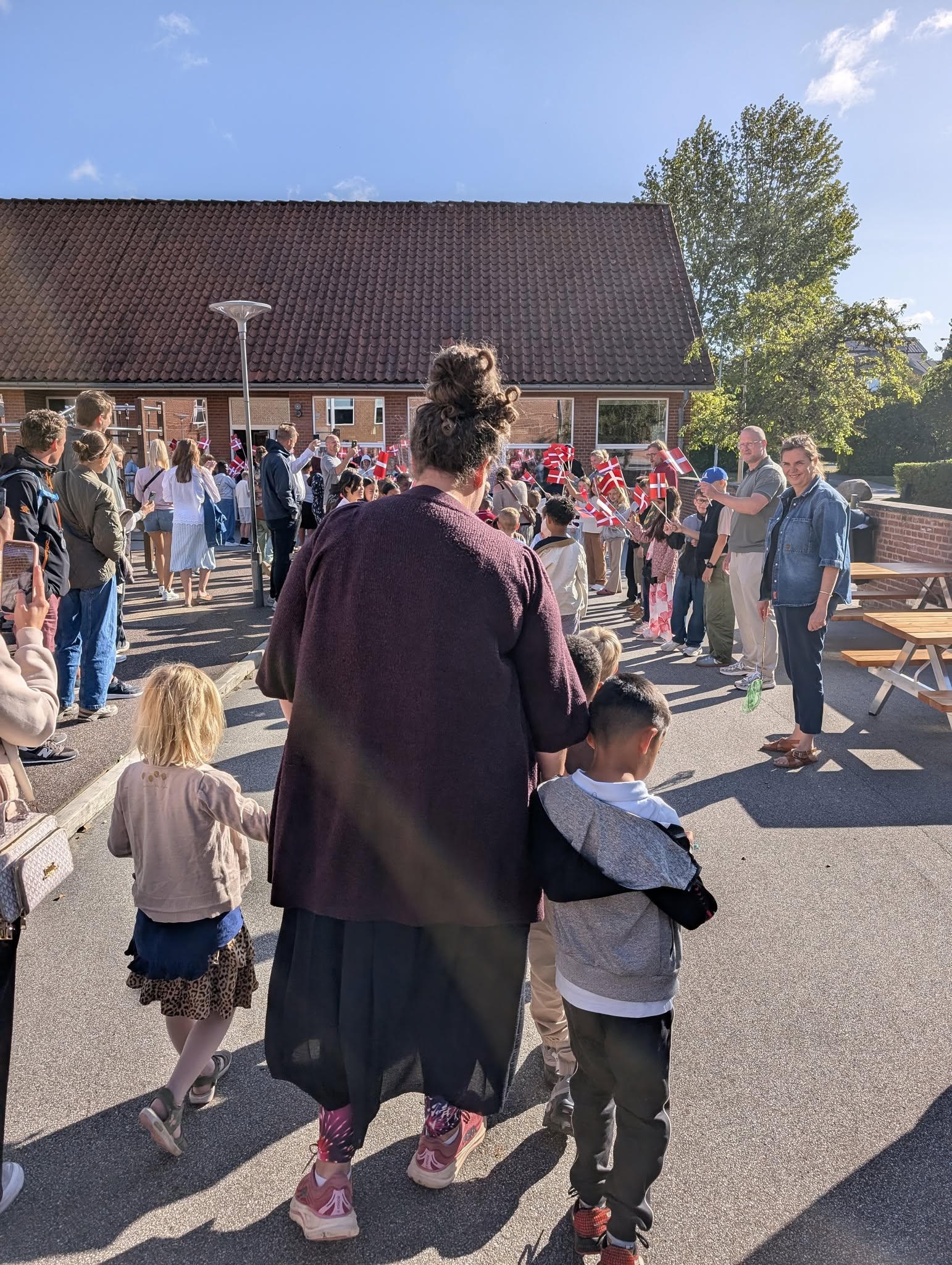 Voksen med to børn i flagalleen på Vestergårdsskolen til første skoledag